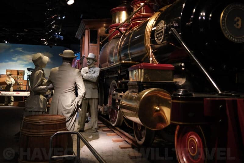 Life-size figures beside a vintage steam locomotive in a museum diorama at ISO 1000 with increasing grain