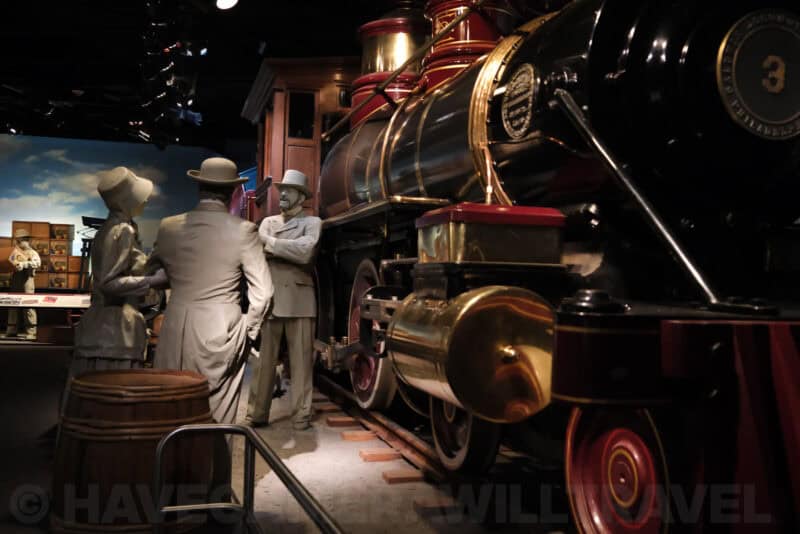 Life-size figures beside a vintage steam locomotive in a museum diorama at ISO 6400 with reduced fine detail