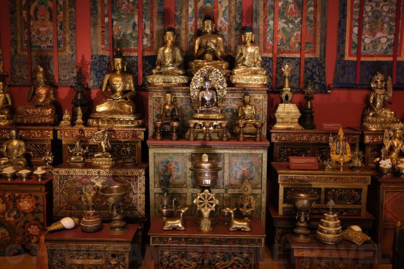 Gilded Buddhist statues and shrine display in a museum exhibit at ISO 250 with faint grain appearing