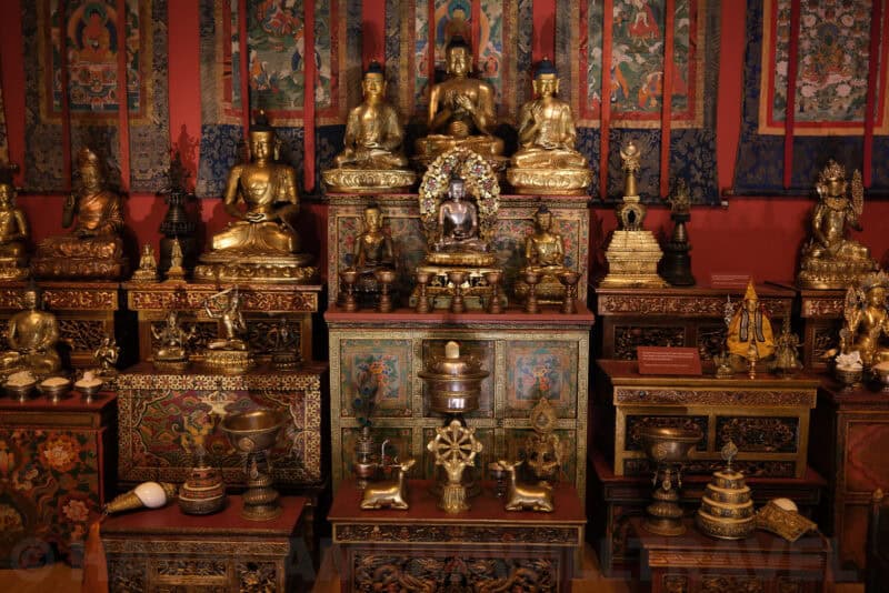 Gilded Buddhist statues and shrine display in a museum exhibit at ISO 320 with subtle noise in shadows