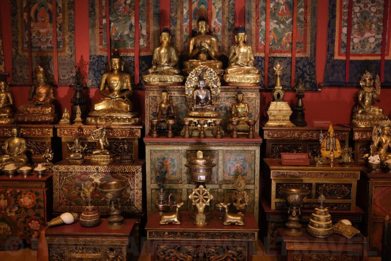 Gilded Buddhist statues and shrine display in a museum exhibit at ISO 400 showing light grain