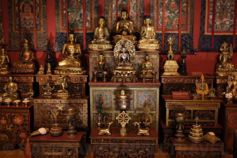 Gilded Buddhist statues and shrine display in a museum exhibit at ISO 800 with visible noise in dark areas
