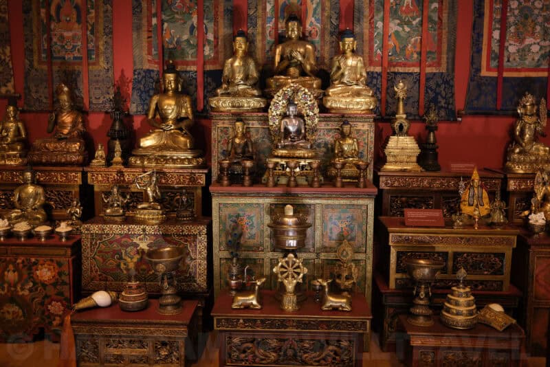 Gilded Buddhist statues and shrine display in a museum exhibit at ISO 1250 with moderate noise