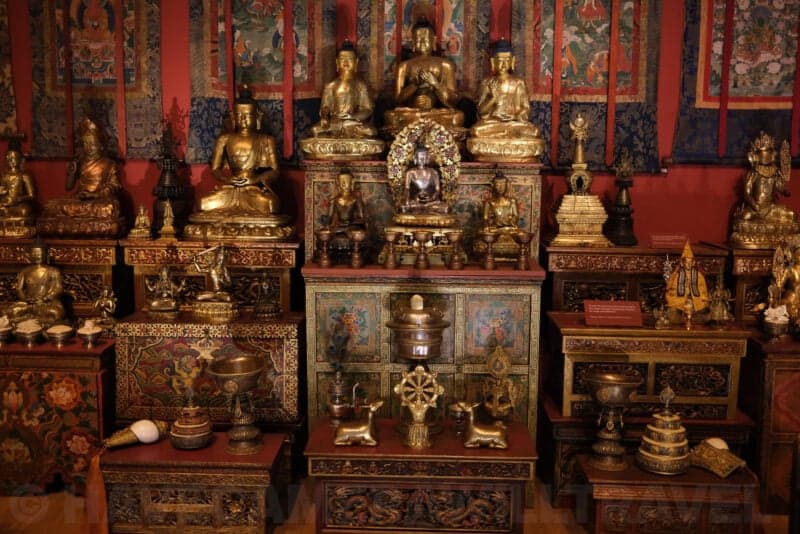 Gilded Buddhist statues and shrine display in a museum exhibit at ISO 2500 with visible high-ISO noise