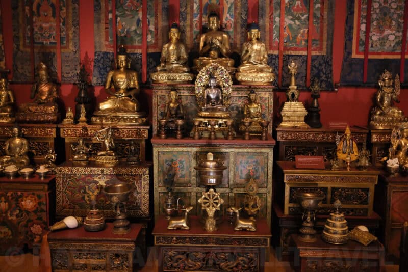 Gilded Buddhist statues and shrine display in a museum exhibit at ISO 8000 with strong grain