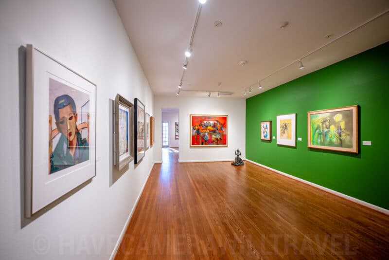 Art gallery hallway with framed paintings on white and green walls above a wood floor