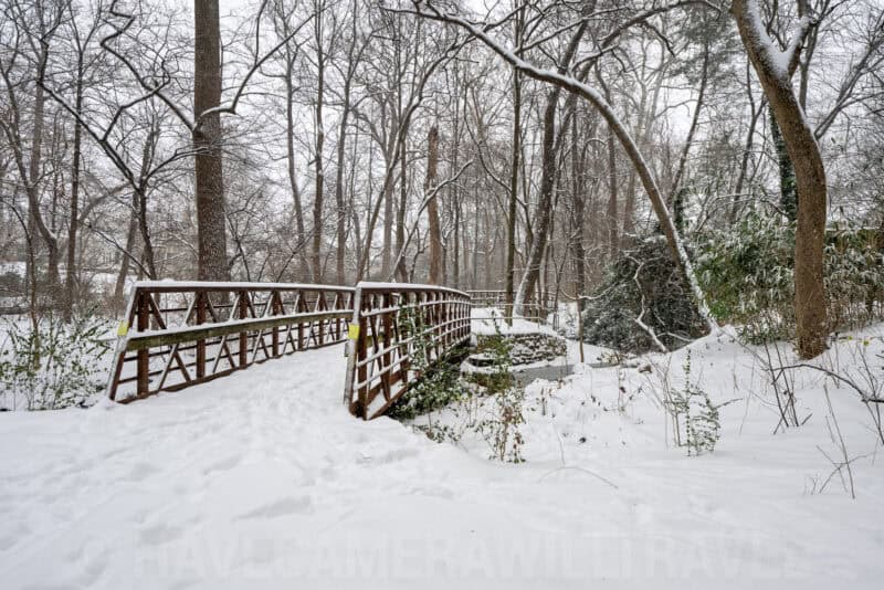 Wooden footbridge crossing a snowy creek surrounded by bare winter trees