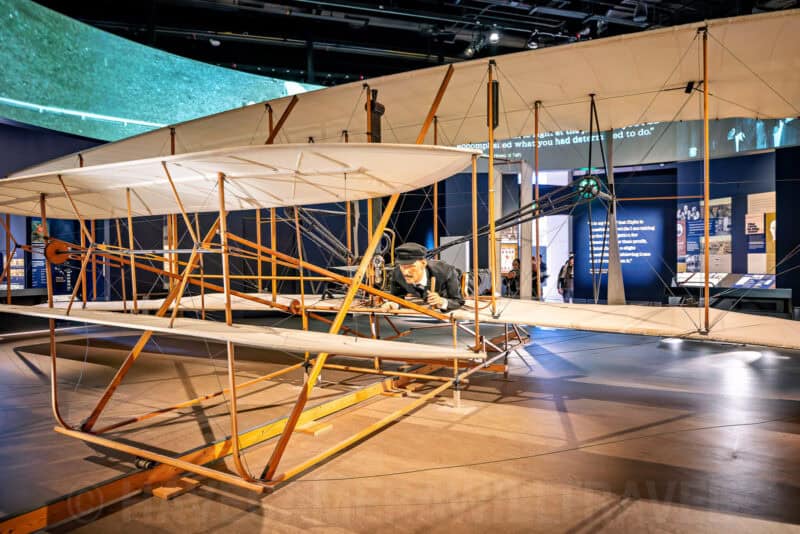 Wright Flyer replica with pilot mannequin on display in an aviation museum exhibit hall
