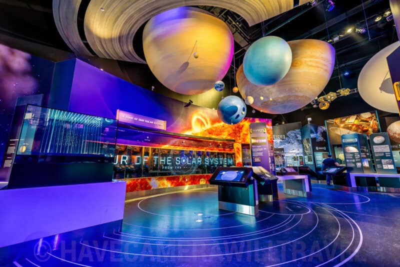 Solar system exhibit with suspended planet models and glowing tour displays in a space museum