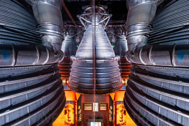 Saturn V rocket engines viewed close-up with symmetrical reflection inside a space museum display