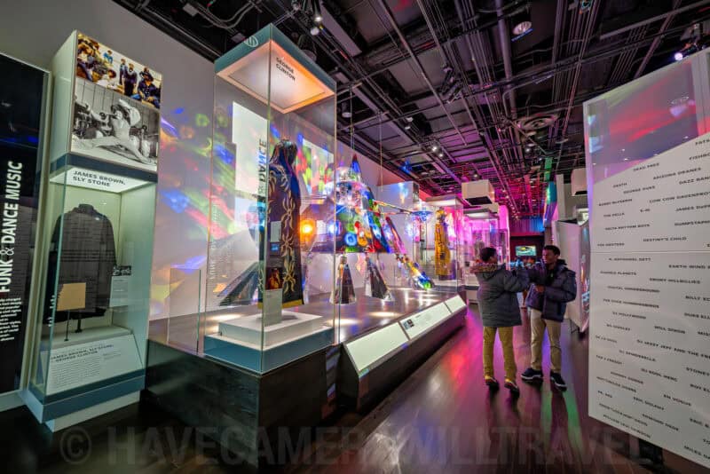 Museum gallery with colorful illuminated costume displays and visitors viewing exhibits