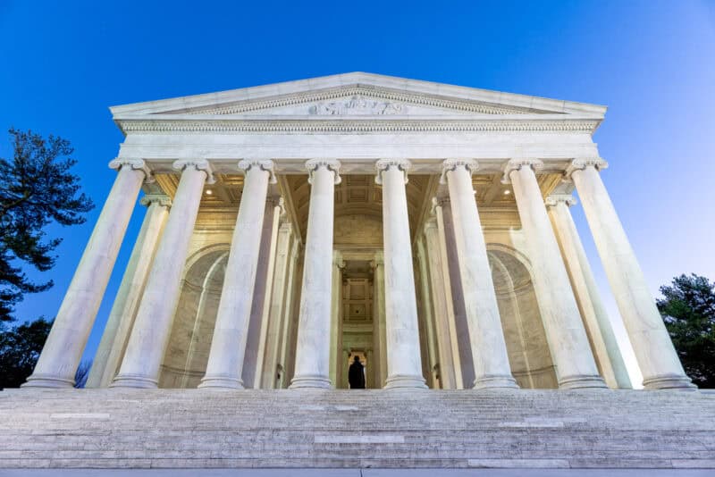 Jefferson Memorial's colonnaded facade and pediment lit at dusk against a blue sky