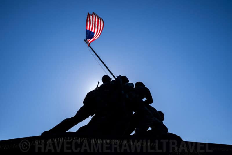 Silhouette of the Iwo Jima Marine Corps War Memorial statue against a blue sky with the American flag