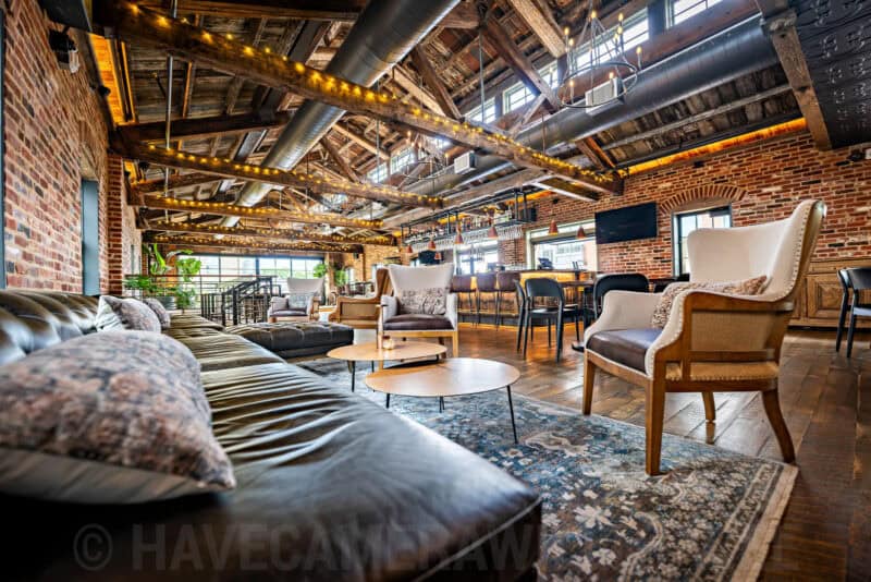 Exposed-brick lounge with leather sofas and string lights beneath timber ceiling beams