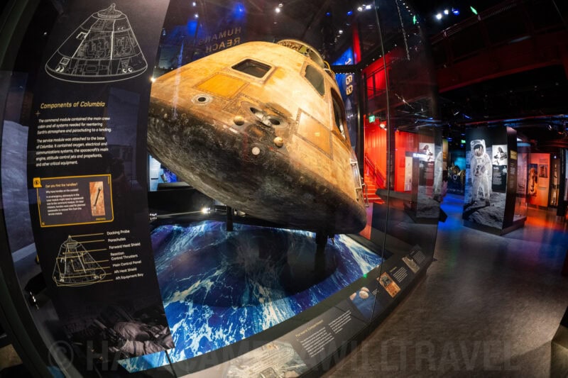 Fisheye close-up of the Apollo command module Columbia on display beside museum exhibit panels
