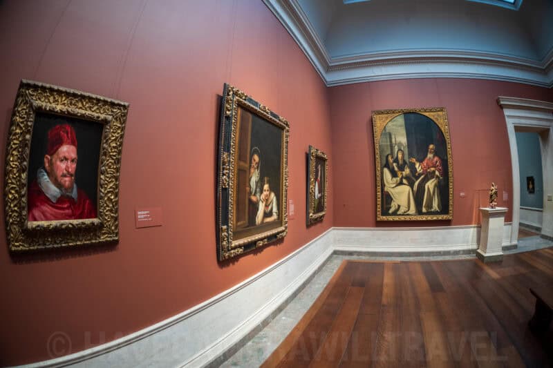 Fisheye view of a red-walled gallery hung with classical portrait paintings in ornate gold frames