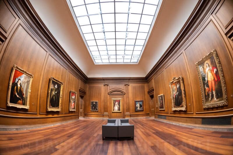 Wood-paneled gallery at the National Gallery of Art with classical portraits lit by an overhead skylight