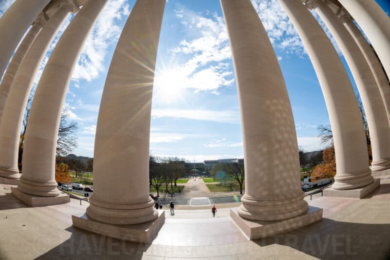 Sunburst through massive stone columns framing a view down the National Mall