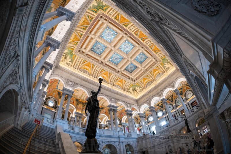 Upward fisheye angle showing a statue and the ornate coffered ceiling inside the Library of Congress