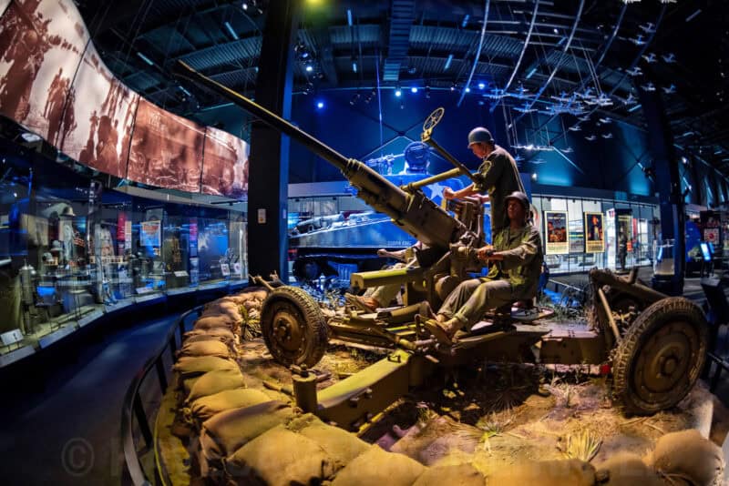 Fisheye view of a WWII anti-aircraft gun diorama with soldier figures in a military museum exhibit