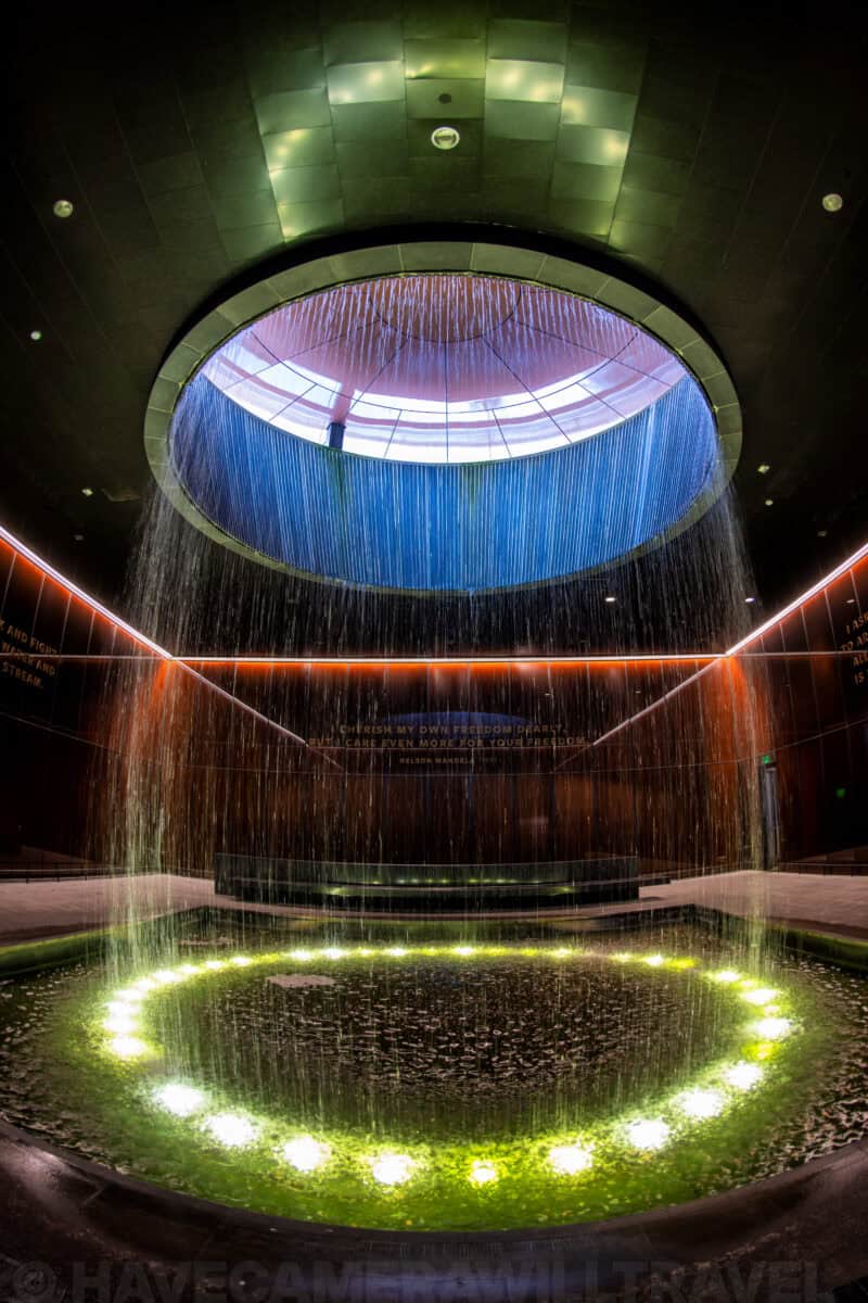 Circular waterfall skylight cascading into a lit pool at a memorial fountain feature