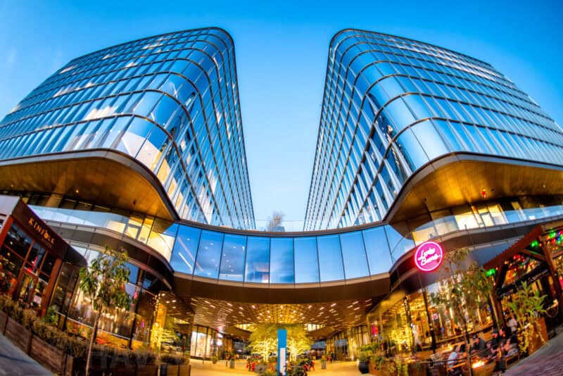 Fisheye shot of curved glass office towers over a shopping plaza at dusk, distorted into a bowl shape