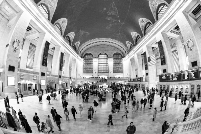 Fisheye interior of Grand Central Terminal's main concourse crowded with travelers, in black and white
