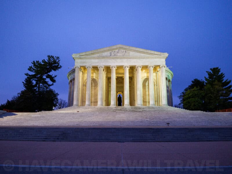 Jefferson Memorial illuminated at dusk with a lone figure standing beneath its columned portico