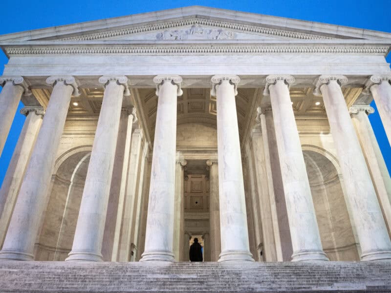 Jefferson Memorial columns viewed from below with a silhouetted figure on the steps at dusk