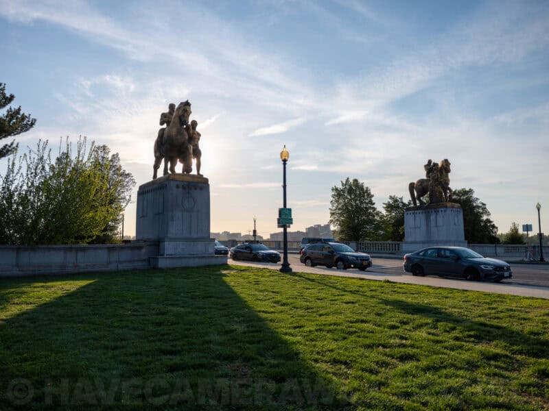 Equestrian bronze statues flanking a roadway on the Arlington Memorial Bridge at sunrise