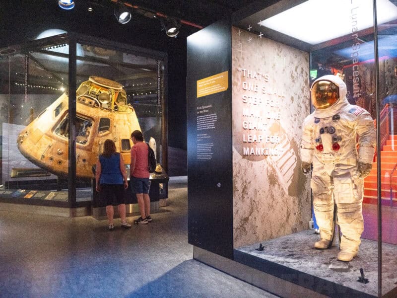Museum visitors viewing an Apollo command module beside a display case with a spacesuit