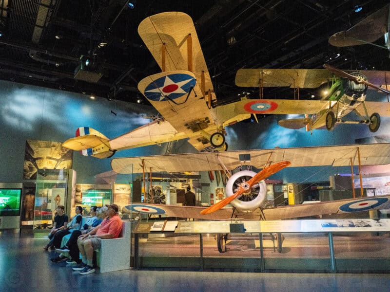 Vintage biplanes suspended above museum visitors seated beneath a World War I aircraft display