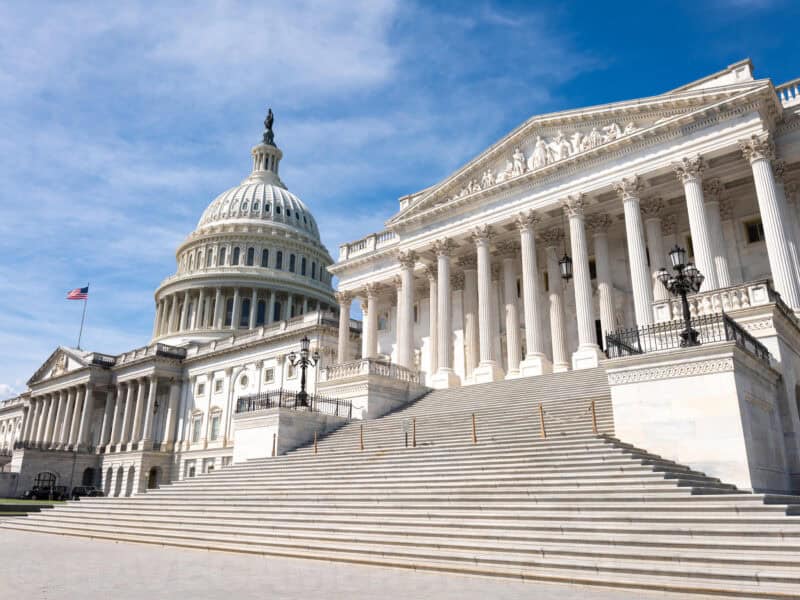 United States Capitol dome and colonnaded facade seen from a low angle against blue sky