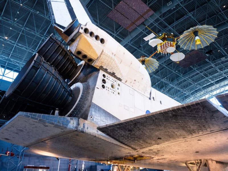 Space shuttle wing and satellite hardware suspended beneath a museum hangar ceiling
