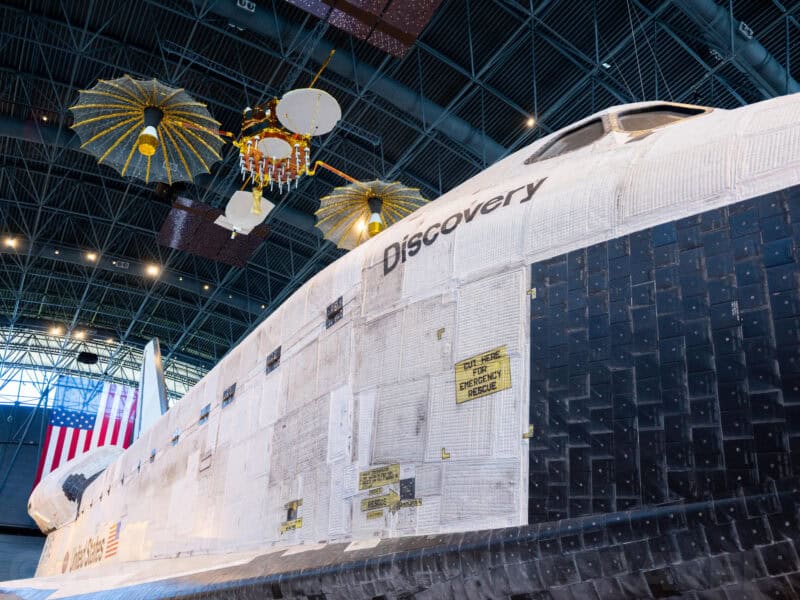 Space shuttle Discovery's nose and cargo bay tiles beneath hanging satellite models