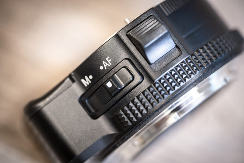 Close-up of the MonsterAdapter LA-FZ1's M and AF focus-mode slider next to a textured release lever