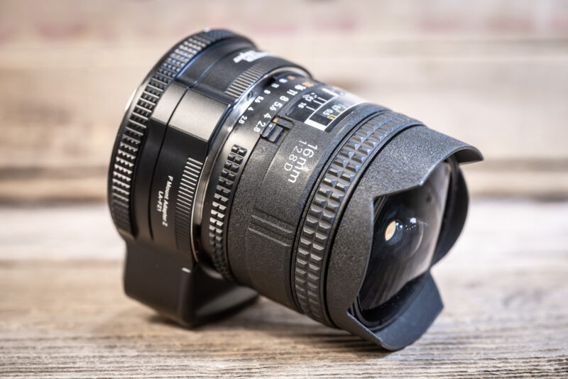 Nikon 16mm f/2.8D fisheye lens with its petal hood mounted on the MonsterAdapter LA-FZ1, angled on a wooden table